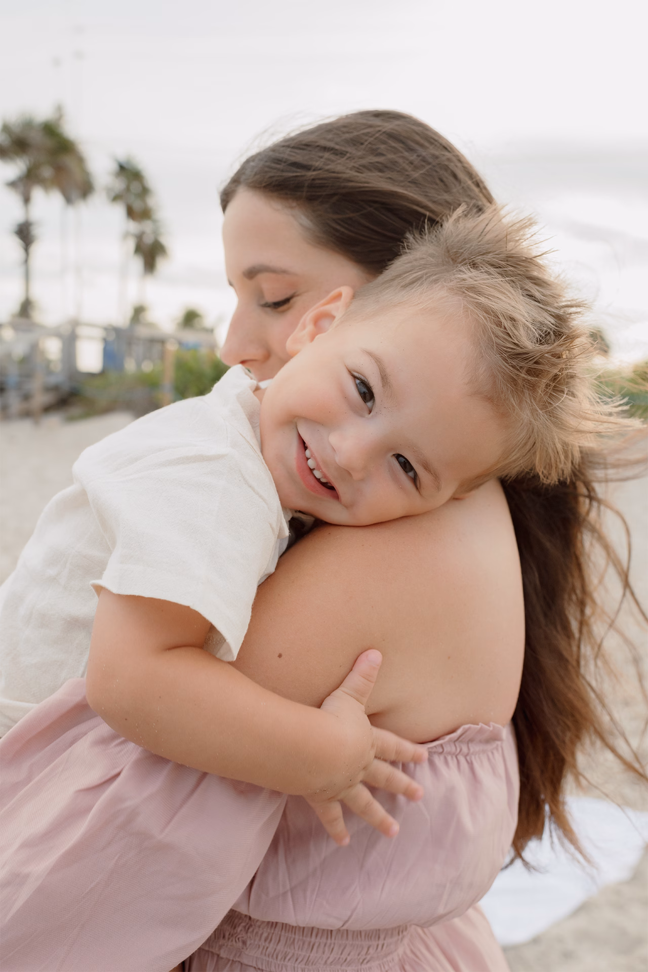 Toddler smiling at the camera leaning in mom shoulder