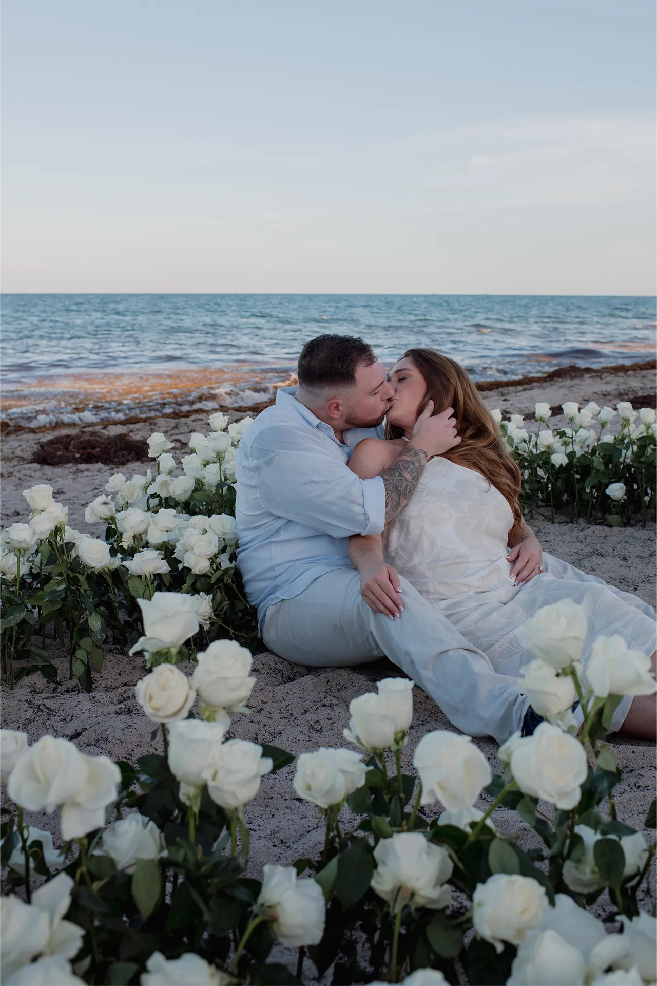 couple kissing surrounded by a field of white roses on the beach