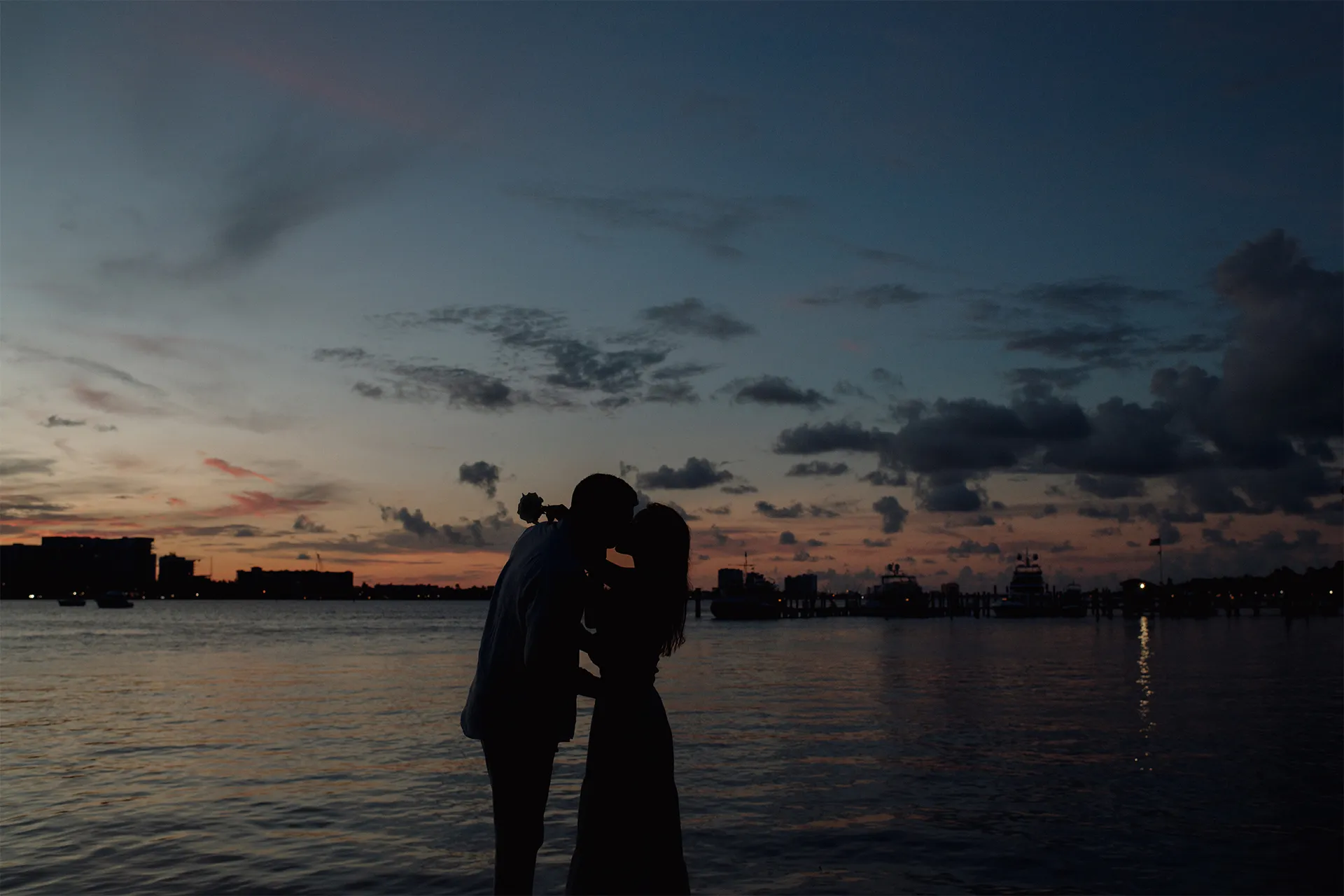 Silhouetted couple kissing at sunset by the water during a beach marriage proposal in Palm Beach.