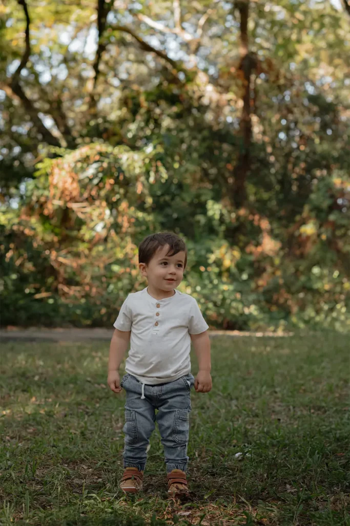 Toddler standing in grassy field surrounded by lush greenery during a natural light family photography session at Tree Tops Park in South Florida