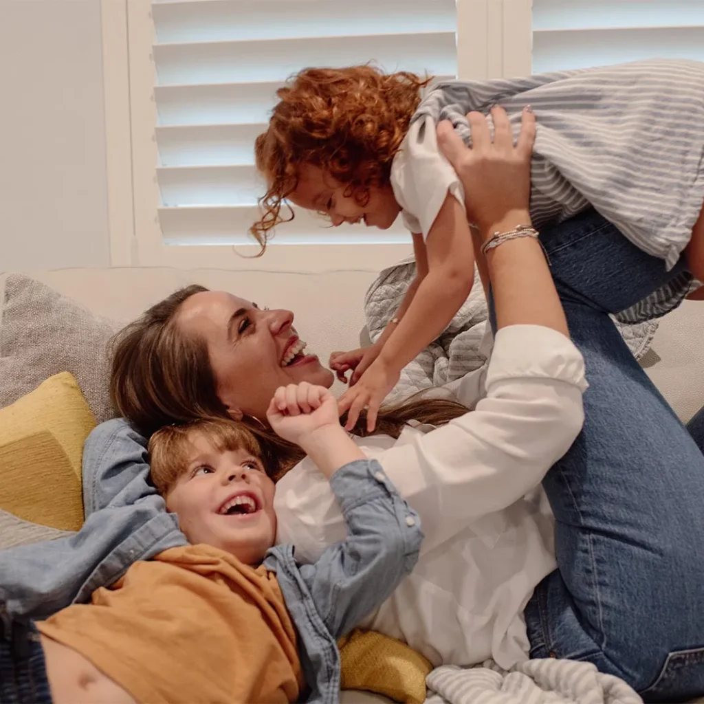 Paula and her two children laughing and playing together on a couch in Fort Lauderdale.