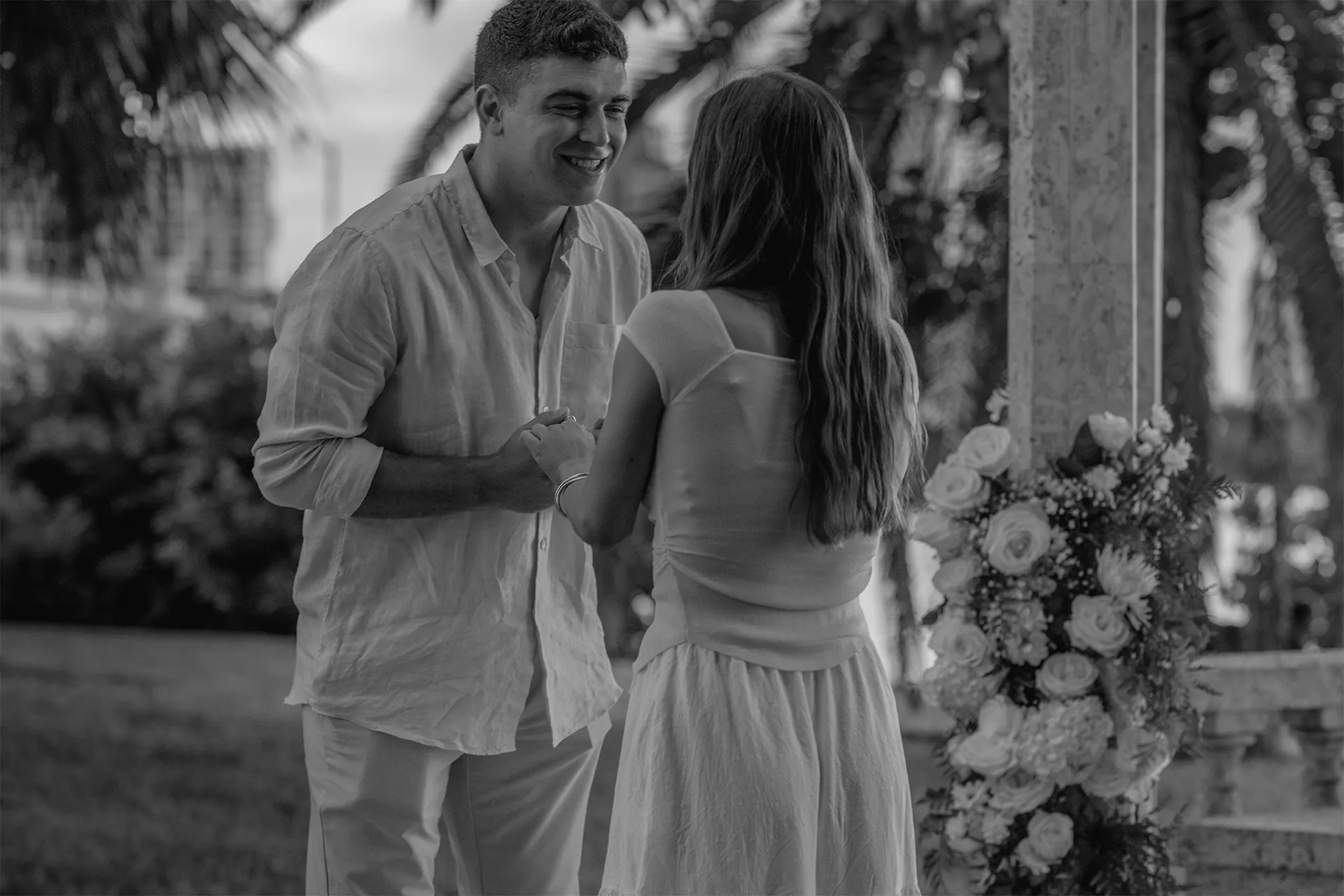 Groom-to-be smiling with fiancée near the floral gazebo during their Palm Beach engagement session