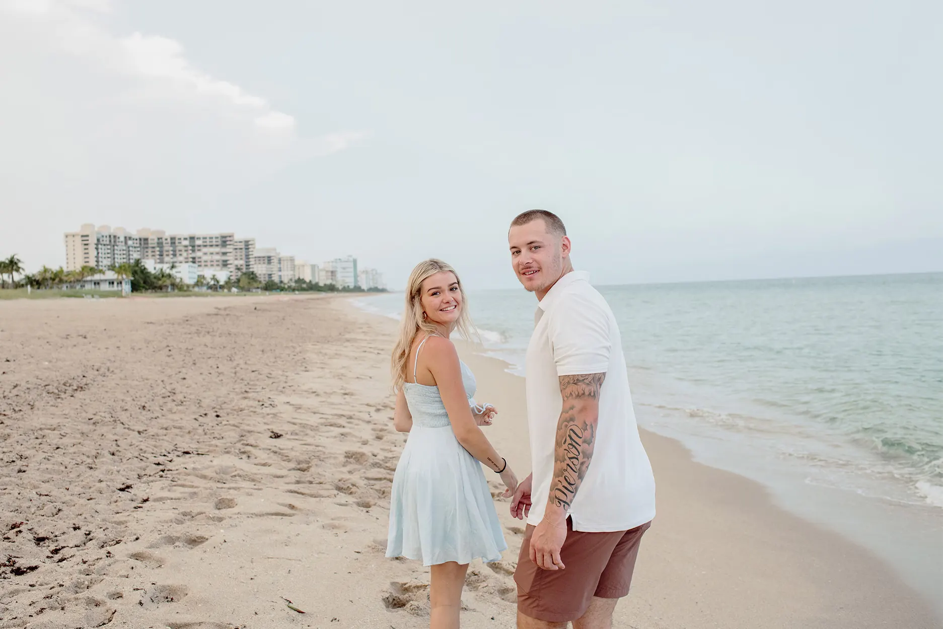 Couple walking away along the shoreline and looking back at the camera smiling