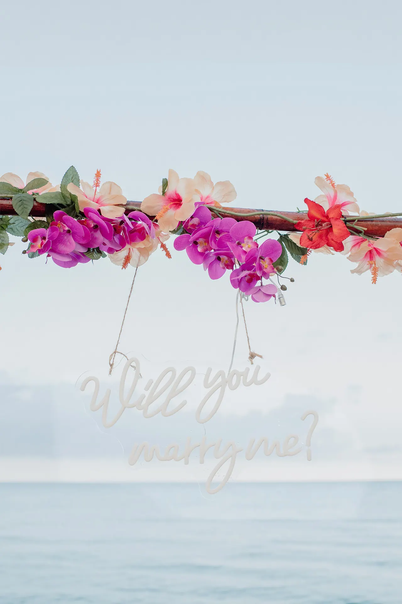 Romantic beach picnic setup featuring a Will You Marry Me neon sign