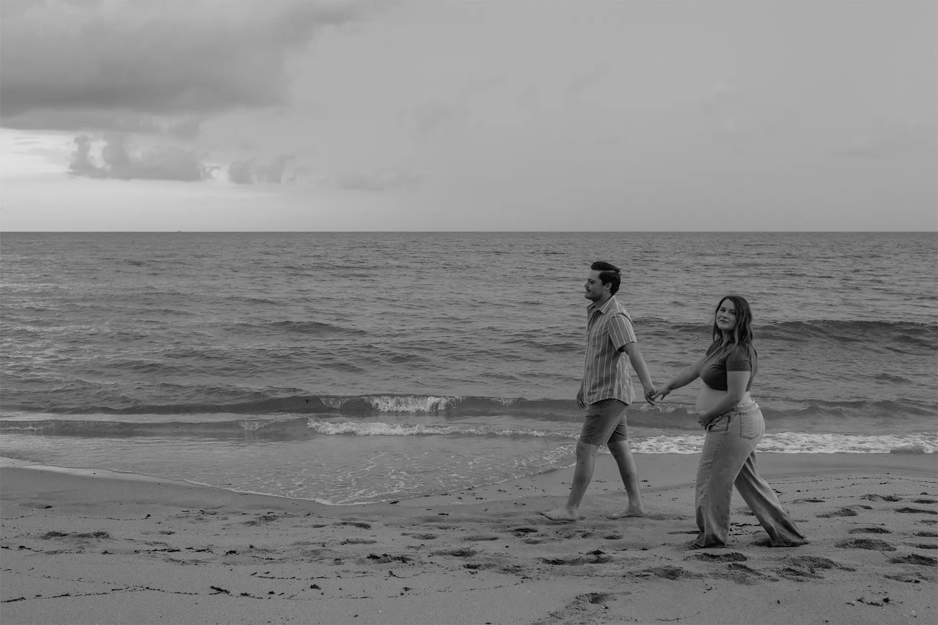 Editorial style couple walking along the beach for their babymoon photography session