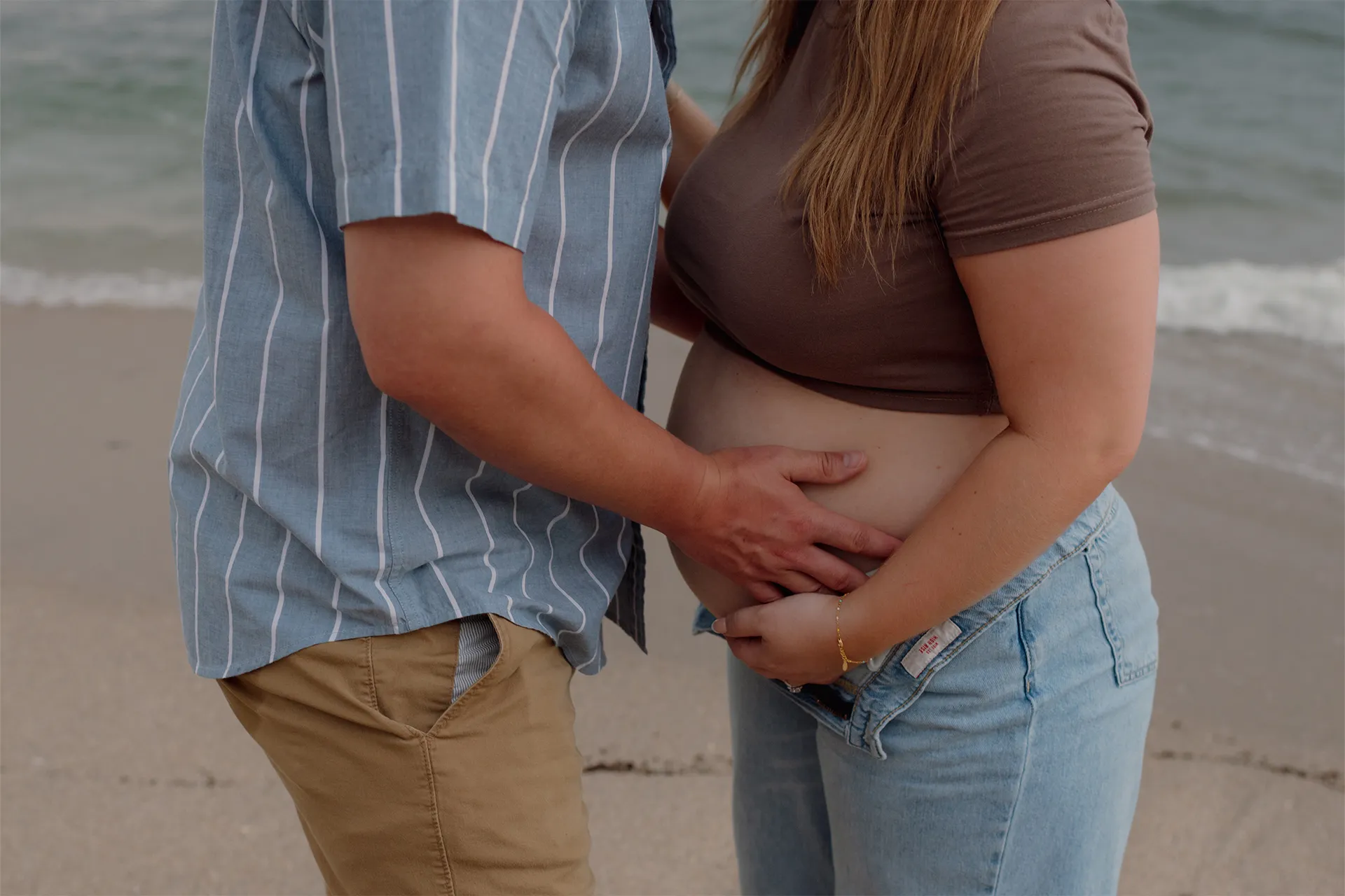 Close up of parents holding the mother's pregnant belly at the beach