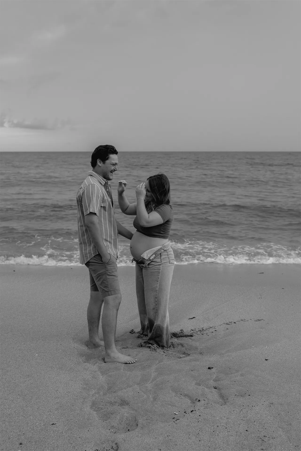 Playful maternity couple facing each other during their beach photography session