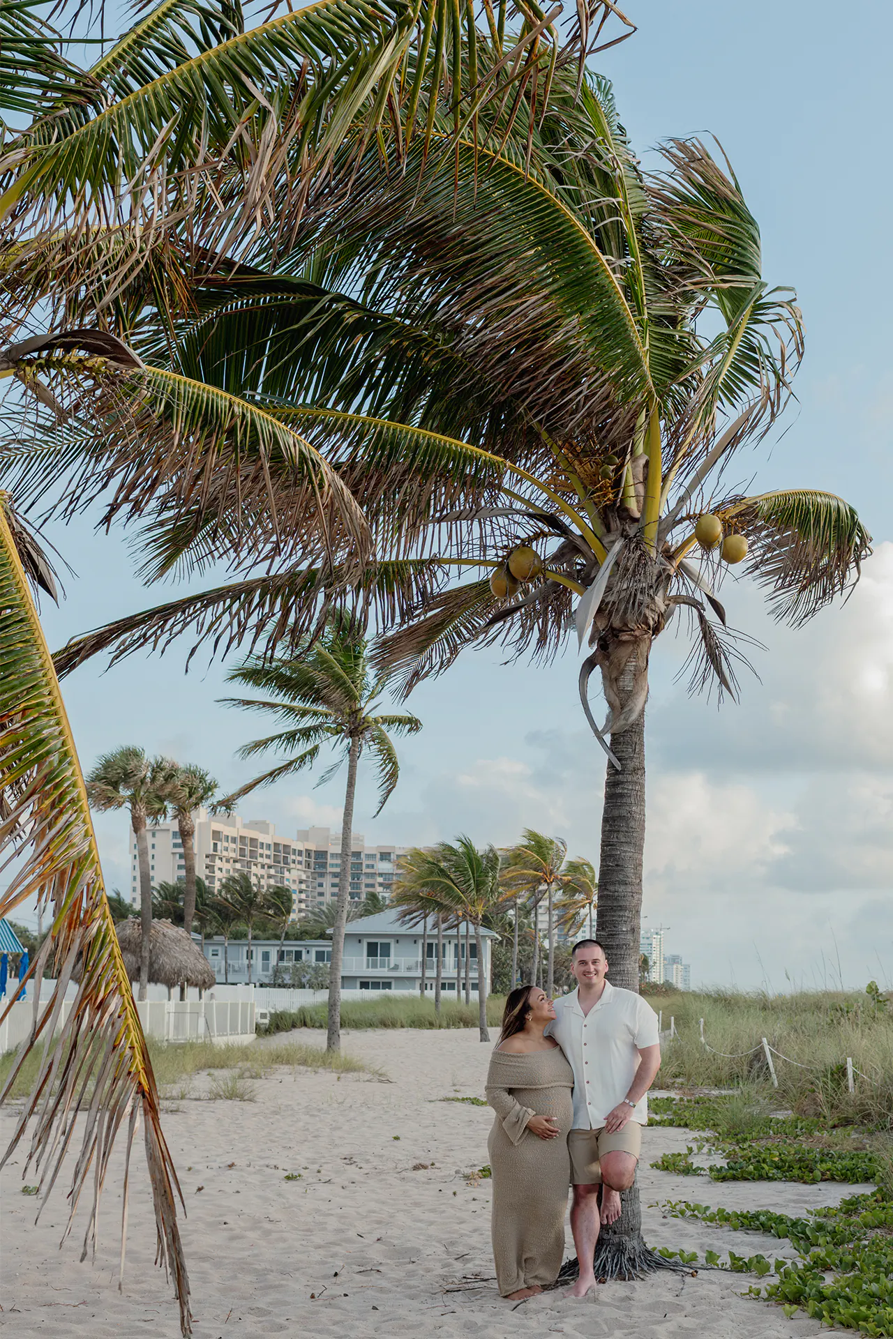 Expecting couple leaning on a palm tree during a Florida beach maternity session