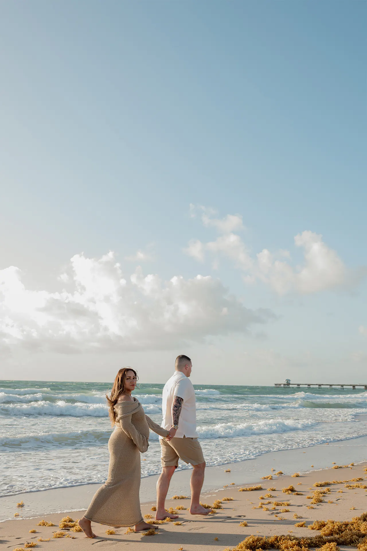Alex and Todd walking along the beachside shore during their pregnancy portraits