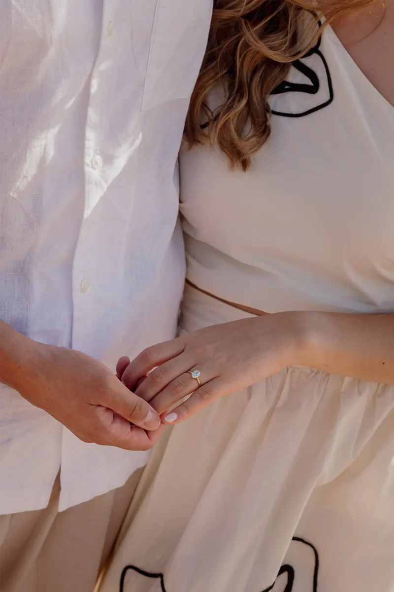 Closeup of a couple holding hands and showing the engagement ring after a sunrise proposal