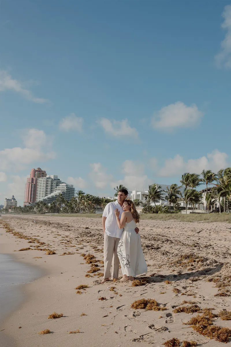 Couple embracing each other and looking towards the ocean after a sunrise engagement session