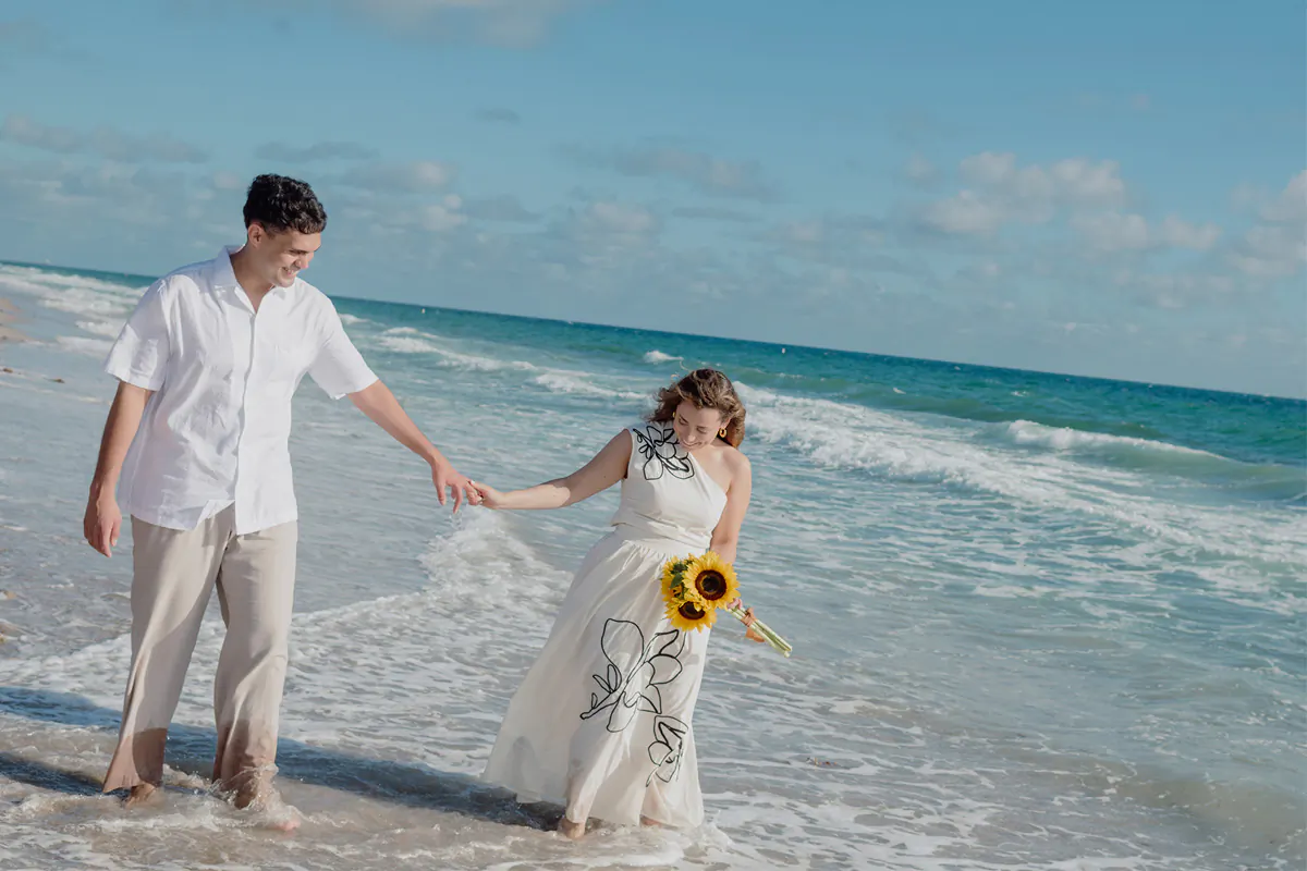 Couple walking in the ocean while holding hands during their sunrise marriage proposal session