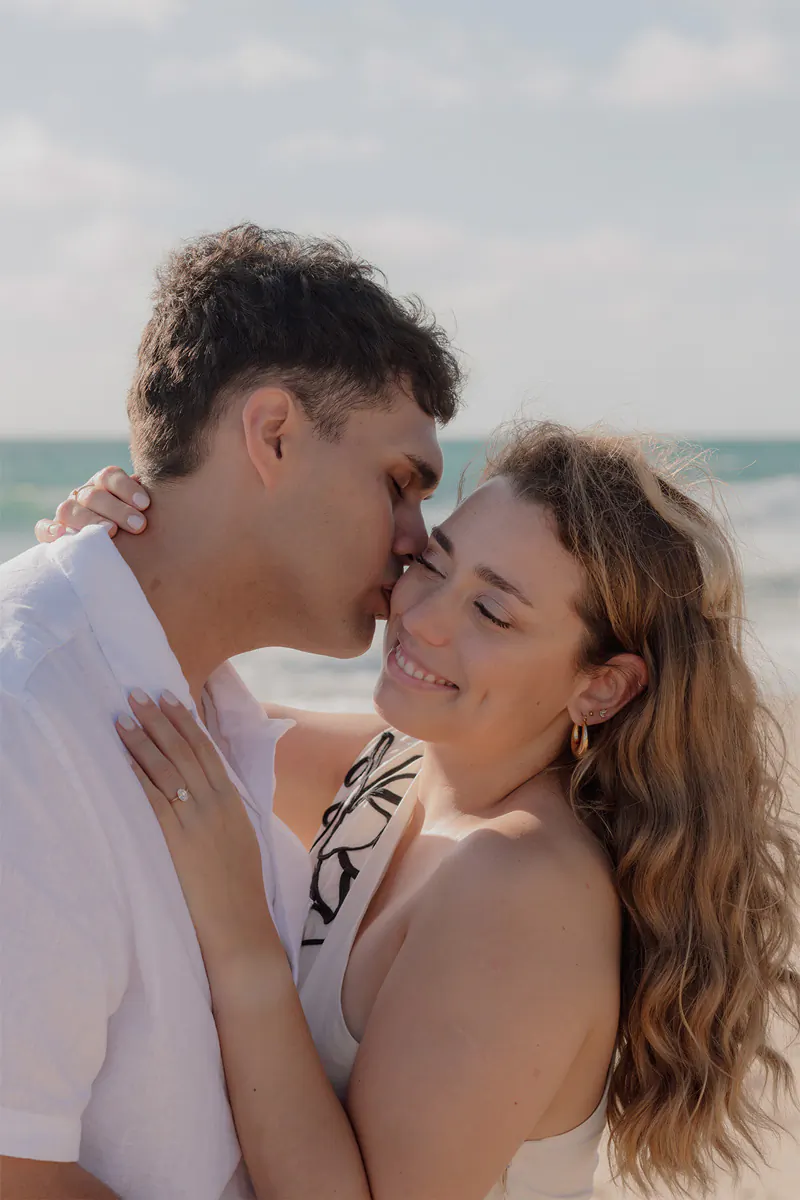 Groom giving a kiss on the cheek to his fiance during their romantic beach engagement session