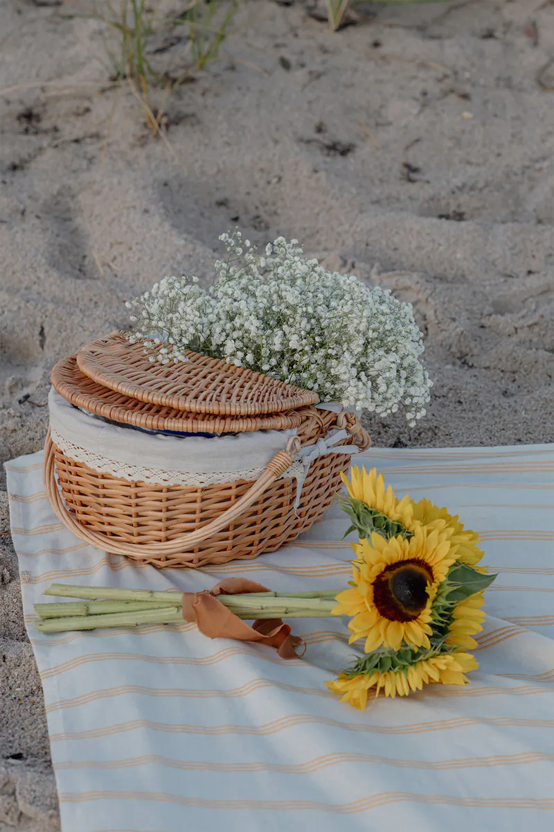 Detail shot of a romantic picnic basket and sunflower bouquet for a beach proposal